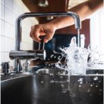 Handyman installing a new chrome faucet in a modern bathroom sink. Faucet installation services for kitchens and bathrooms in Surrey, BC